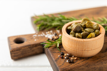 Capers in a bowl on a wooden kitchen table. Capers with sea salt and rosemary. Pickled capers.Mediterranean cuisine ingredient. Organic spices and seasonings. Copy space.
