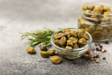 Capers in a bowl on a wooden kitchen table. Capers with sea salt and rosemary. Pickled capers.Mediterranean cuisine ingredient. Organic spices and seasonings. Copy space.