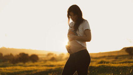 Woman happy for her motherhood posing in a sunset in nature pregnant for a few months looking and caressing her belly. Motherhood concept, blurred background and copy space