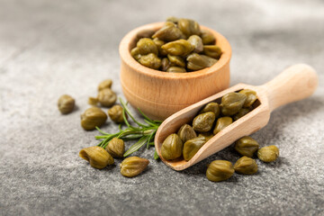 Capers in a bowl on a wooden kitchen table. Capers with sea salt and rosemary. Pickled capers.Mediterranean cuisine ingredient. Organic spices and seasonings. Copy space.
