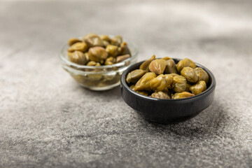 Capers in a bowl on a wooden kitchen table. Capers with sea salt and rosemary. Pickled capers.Mediterranean cuisine ingredient. Organic spices and seasonings. Copy space.