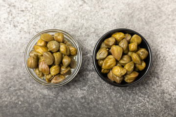 Capers in a bowl on a wooden kitchen table. Capers with sea salt and rosemary. Pickled capers.Mediterranean cuisine ingredient. Organic spices and seasonings. Copy space.