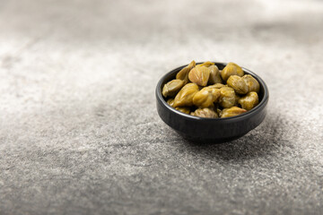 Capers in a bowl on a wooden kitchen table. Capers with sea salt and rosemary. Pickled capers.Mediterranean cuisine ingredient. Organic spices and seasonings. Copy space.