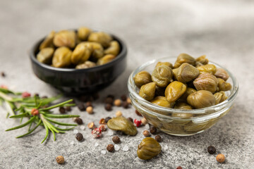 Capers in a bowl on a wooden kitchen table. Capers with sea salt and rosemary. Pickled...