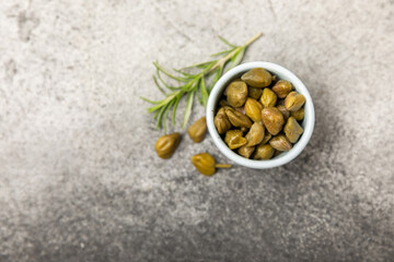 Capers in a bowl on a wooden kitchen table. Capers with sea salt and rosemary. Pickled capers.Mediterranean cuisine ingredient. Organic spices and seasonings. Copy space.