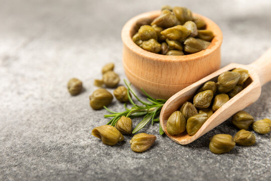 Capers in a bowl on a wooden kitchen table. Capers with sea salt and rosemary. Pickled capers.Mediterranean cuisine ingredient. Organic spices and seasonings. Copy space.