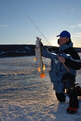 Ice angler fishing for pike at sunset 
