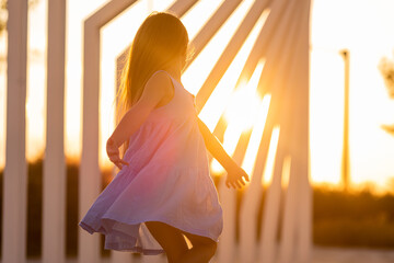 beautiful little girl with long brown hair walks at sunset in the city park in summer