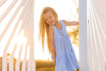 beautiful little girl with long blonde hair walks at sunset in the city park in summer