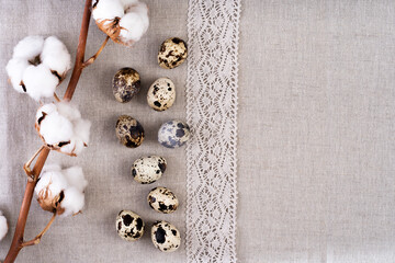 Composition with Easter eggs on textile linen fabric and cotton branches. Texture of linen fabric with quail eggs.