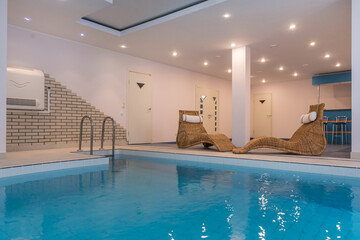 A bright room with a blue swimming pool and rattan sun beds for relaxation.