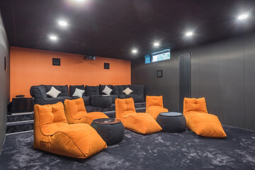 The interior of a home theater with gray walls and flooring. A large grey sofa and orange armchairs.