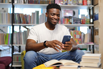 Young man using a smartphone in a library, seamlessly blending modern technology with academic...
