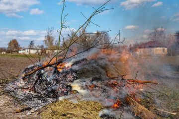 An outdoor fire burns with a house in the background. Illegal burning of leaves and dry grass.