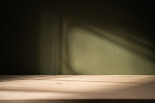 Empty table on khaki green texture wall background. Composition with abstract shadows on the wall and light reflections. Mock up for presentation, branding products, cosmetics food or jewelry.	