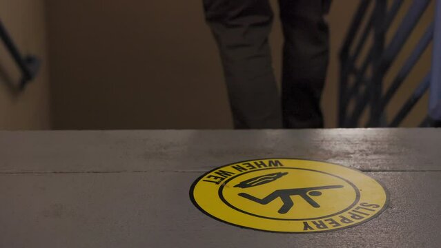 man walks down stairs past a slippery when wet sign on floor