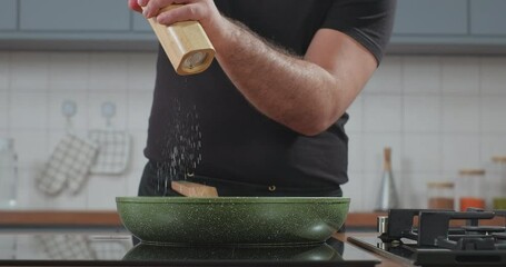 Chef hands grinding salt on the dish. Male chef salting dish in a frying pan with a hand salt mill in slow motion