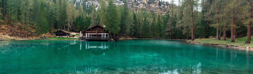 Fototapeta na wymiar Panoramic view of turquoise water alpine lake Ghedina with restaurant in Dolomiti mountains, Cortina dAmpezzo, Italy ii springtime. Small lake in the forest in Dolomites in Italian Alps