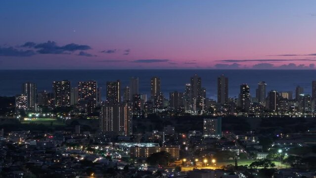 Downtown Waikiki sunset views. Cinematic aerial above Honolulu capital of Hawaii state, USA. Scenic pink purple sunset sky above city illuminated at night. Modern cityscape of Oahu island in Pacific