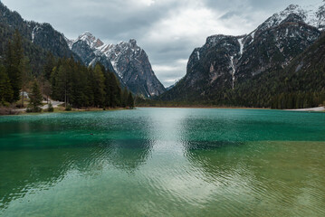 Moody landscape with turquoise water alpine lake Lago di Dobbiaco in Dolomites mountains, Cortina dAmpezzo, Italy on cloudy spring day. Lake Toblacher See in the forest in Dolomiti