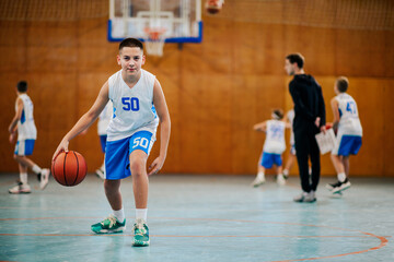 A young basketball kid is dribbling a ball on court on training.