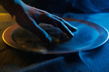 Terrible hand over a bowl of magical liquid. Colored smoke moves beautifully against on a dark background. Fortune teller, mind power, prediction, halloween concept.