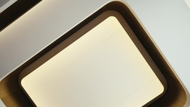 Low angle view of stretch multi-level ceiling decorated with wooden panels and original square-shaped led lamp in center. Stylish lighting design in modern interior