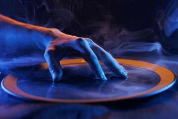 Terrible hand over a bowl of magical liquid. Colored smoke moves beautifully against on a dark...