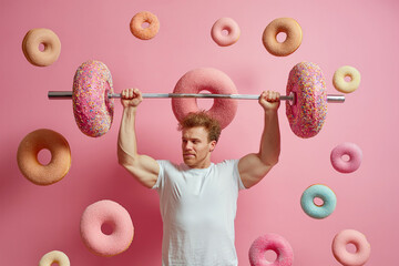 Man trying to lift a barbell made of big donuts. Dumbbell doughnut. Creative concept for a healthy lifestyle, Bad fitness nutrition, sport and bodybuilding. Weight training, wrong diet, funny food - obrazy, fototapety, plakaty