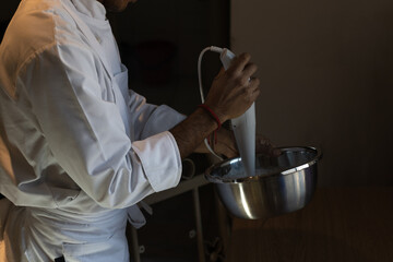 Photograph of a male pastry chef in an apron churning cream in a bowl for the preparation of a cake at home for a birthday celebration