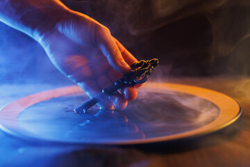 Hand with a mysterious key in a bowl of magic liquid. Colored smoke moves beautifully against on a...