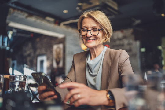 Mature Blonde causacian Woman use Smartphone at Cafe while sit alone