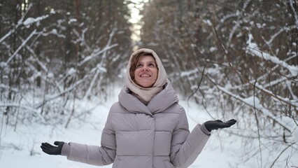 A young woman stands against a background of fir trees under a snowy forest in winter. A girl in a...