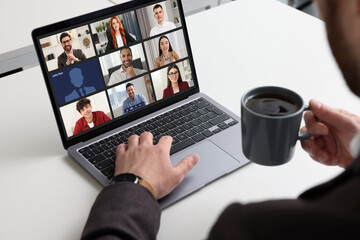 Man having video chat with coworkers via laptop at white table, closeup