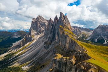 Bare peak and steep slopes of Seceda mountain range against cloudy sky. Observation deck overlooking giant ridgeline in Alps aerial view