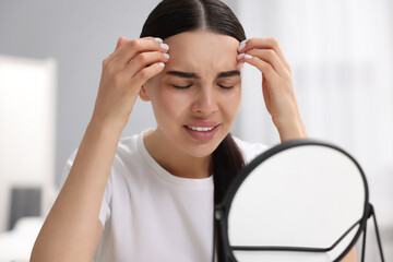 Woman with dry skin looking at mirror indoors