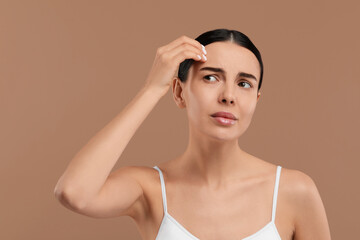 Woman with dry skin checking her face on beige background