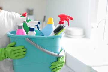 Woman holding bucket with cleaning supplies in kitchen, closeup