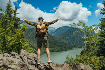 Hiking traveller man with backpack hands up enjoying beautiful view of Lake Ritsa in Abkhazia