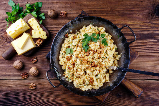 Traditionelle Allg&auml;uer K&auml;sesp&auml;tzle mit Waln&uuml;ssen serviert als Draufsicht in einer schmiedeeisernen Pfanne auf einem rustikalen Holzboard auf einer Bergh&uuml;tte