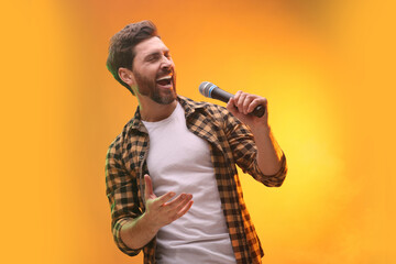 Handsome man with microphone singing on golden background