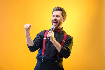 Emotional man with microphone singing on yellow background