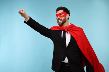 Businessman wearing red superhero cape and mask on light blue background