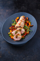 Gebratenes Mangalica Schweinefilet gef&uuml;llt mit gehackten Walln&uuml;ssen und K&uuml;rbis und umwickelt mit Speckmantel serviert mit Gem&uuml;se als close-up auf Design Teller 