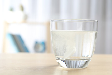 Glass of water with effervescent tablet on wooden table indoors, space for text