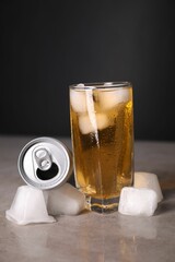 Tasty energy drink with ice cubes in glass and aluminium can on grey table