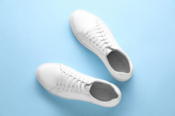 Pair of stylish white sneakers on light blue background, top view