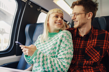 A hipster couple is sitting in train and using phone while traveling.