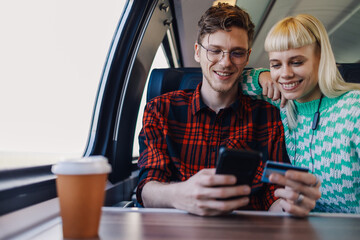 Couple in train is using a credit card and phone for online shopping.