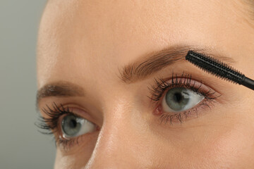 Fototapeta premium Woman applying mascara on grey background, closeup